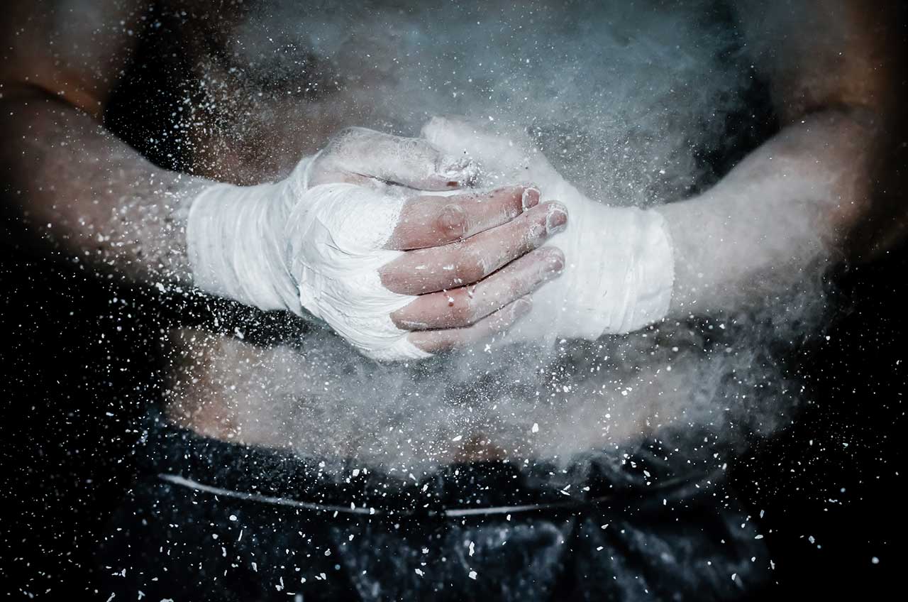 Athlete with taped hands clapping chalk dust into the air before training or competition.