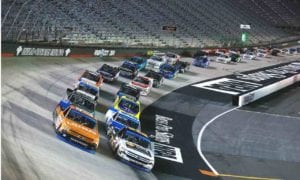 Race trucks speeding around a curve on a brightly lit NASCAR track