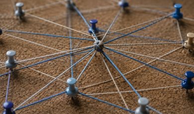 A corkboard displaying a network of strings connected to various colored pushpins, symbolizing a complex web of connections.